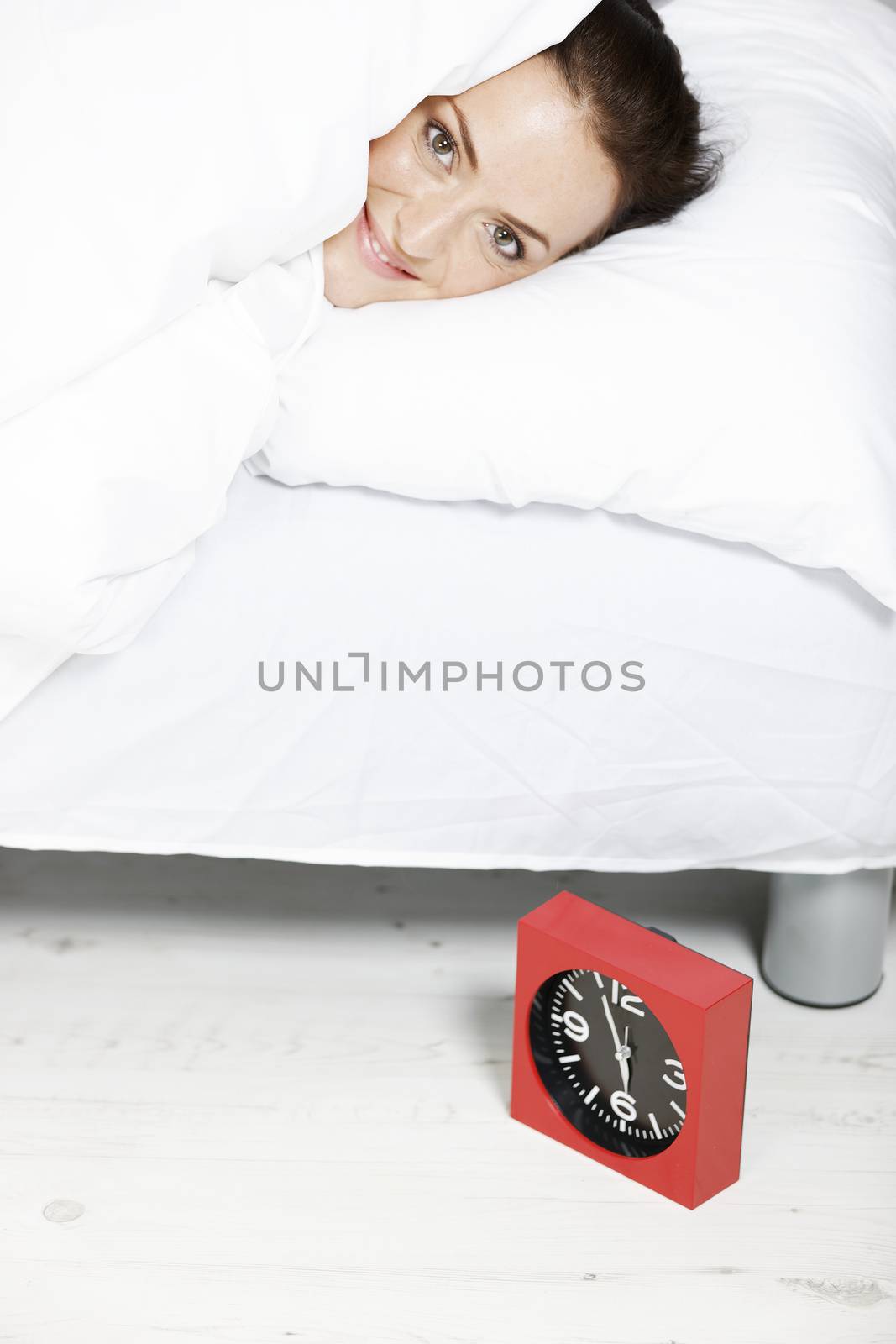 young woman in bed waking up by her clock