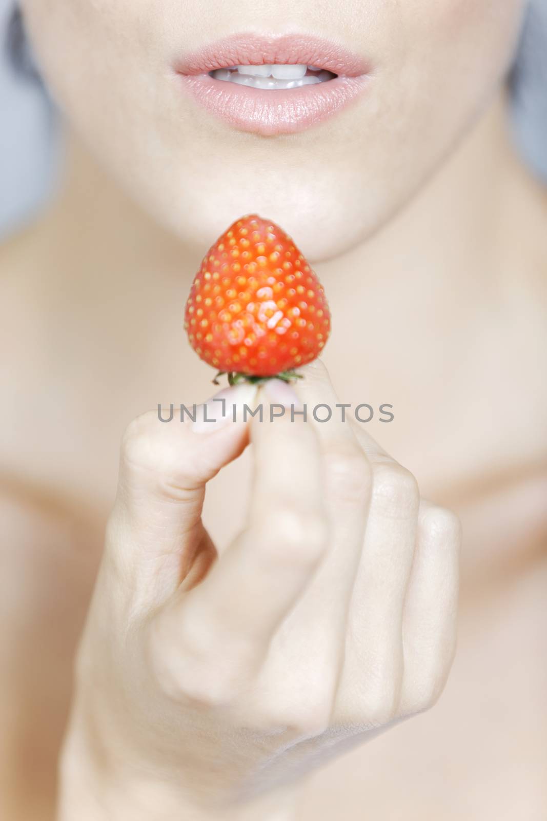 Young woman holding a strawberry in a beauty style pose.