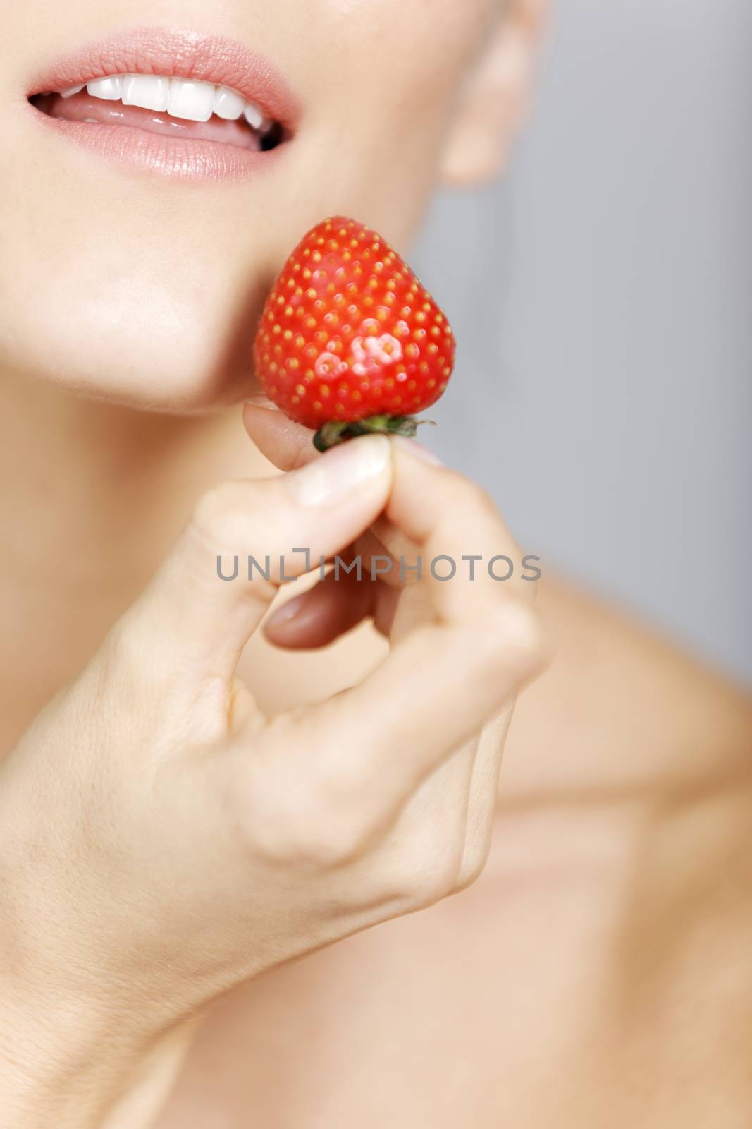 Young woman holding a strawberry in a beauty style pose.