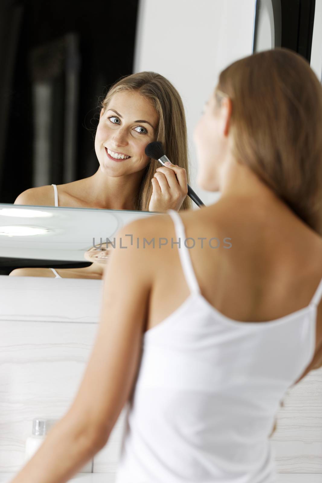 Attractive young woman in underwear applying make up in bathroom.