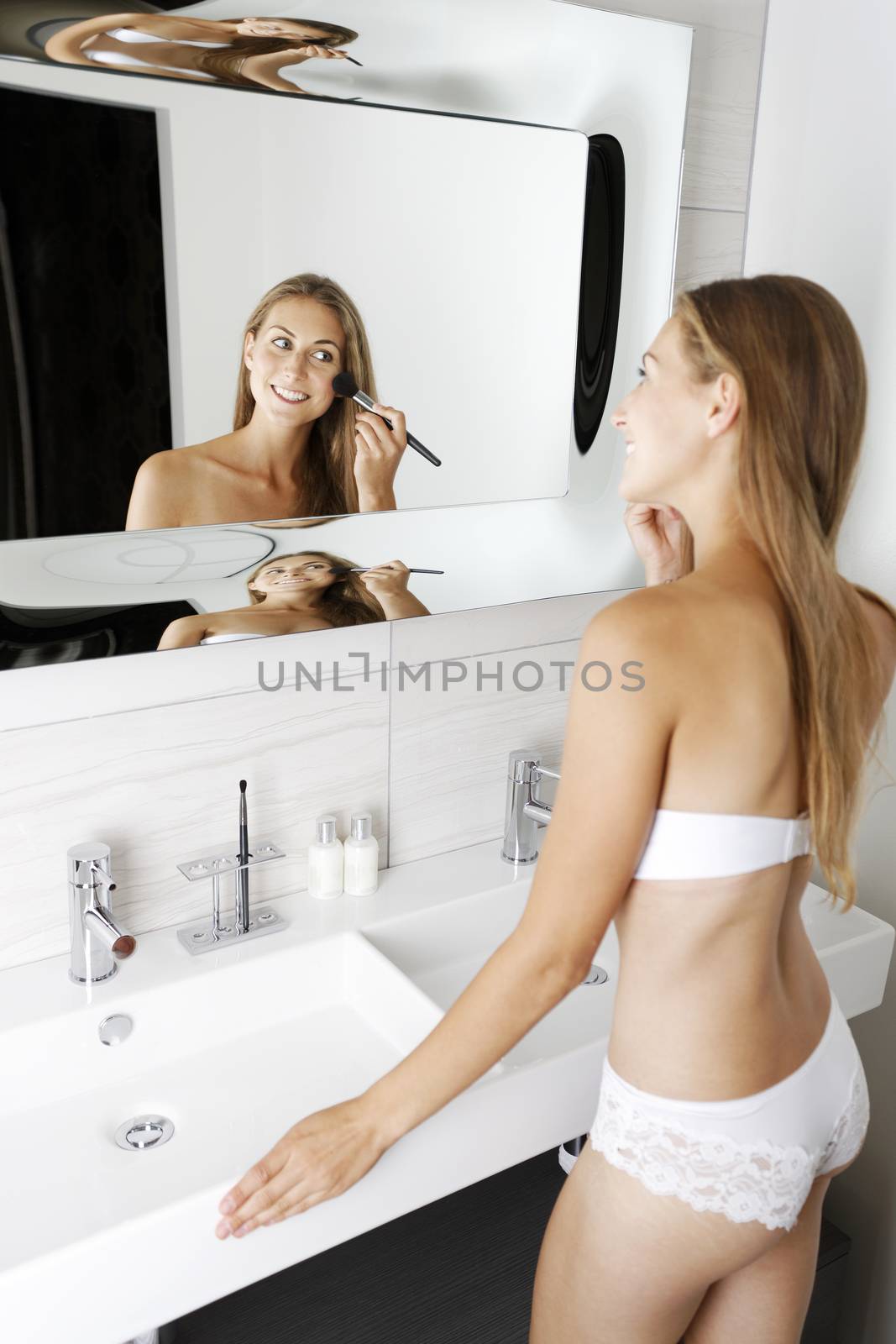 Attractive young woman in underwear applying make up in bathroom.