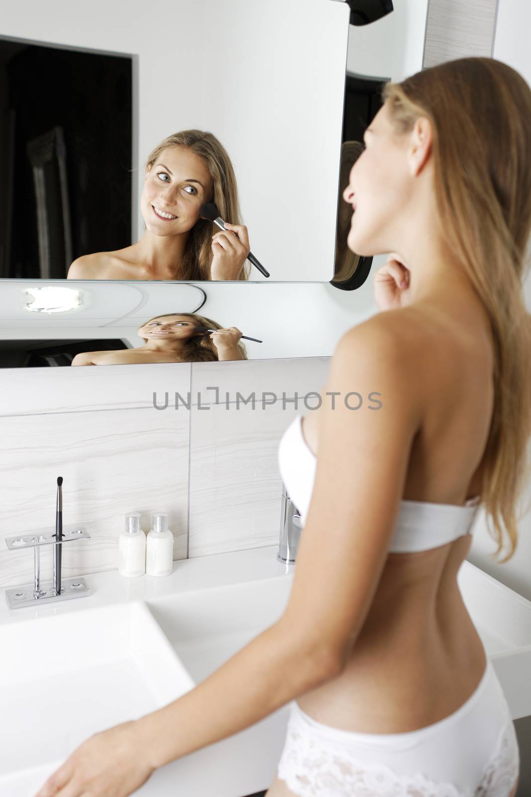 Attractive young woman in underwear applying make up in bathroom.