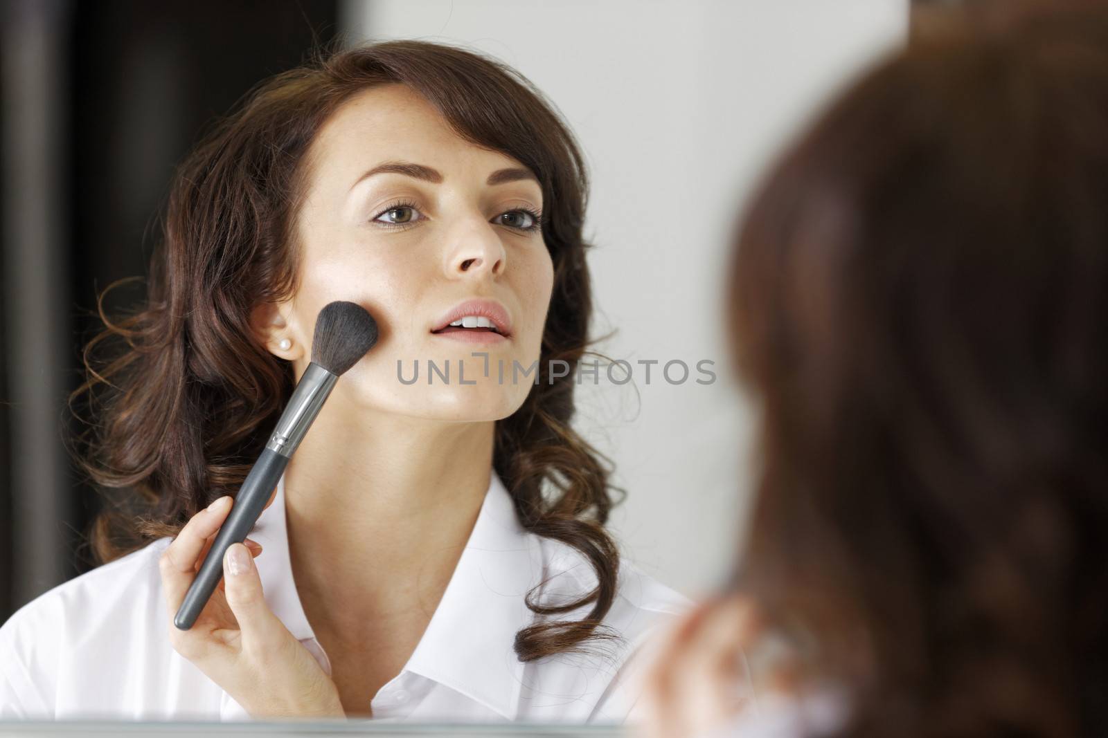 Attractive young woman doing her makeup in front of the bathroom mirror.