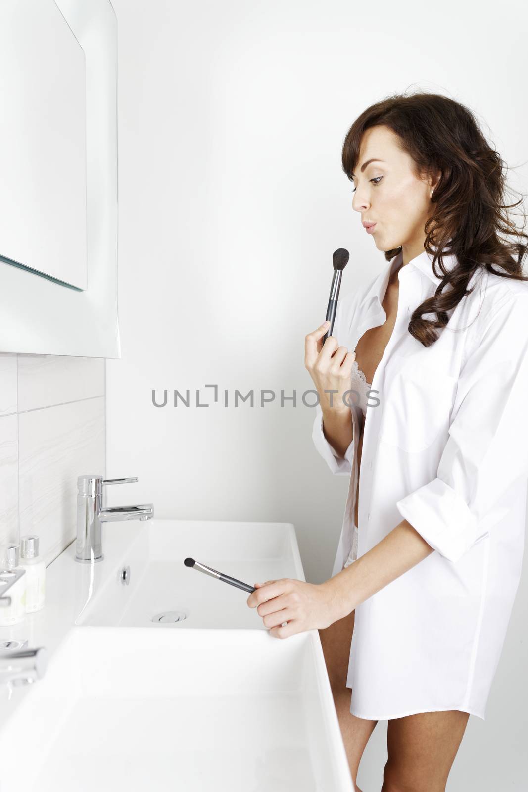 Attractive young woman doing her makeup in front of the bathroom mirror.