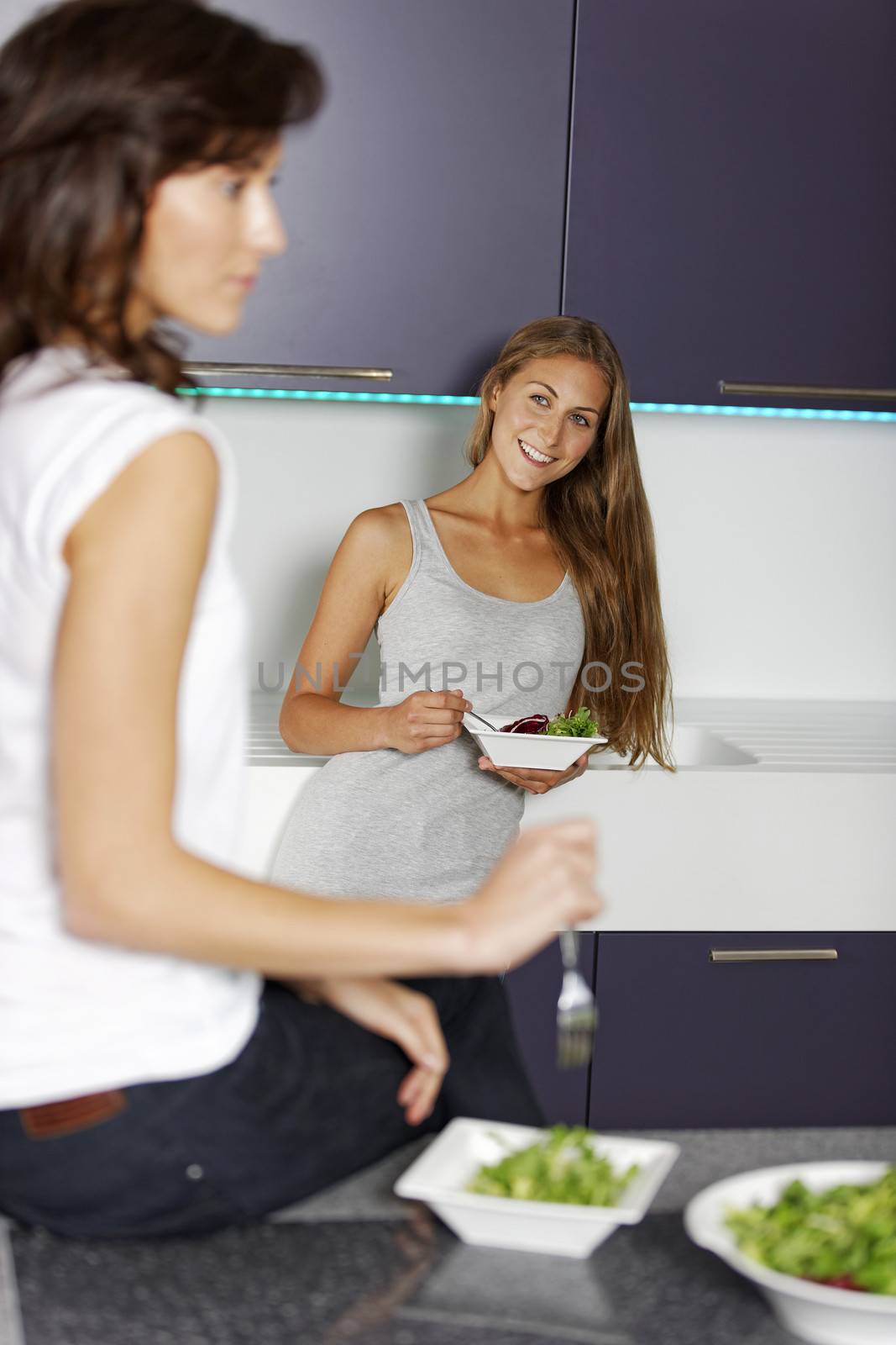 Two happy friends enjoying a fresh salad in their kitchen.