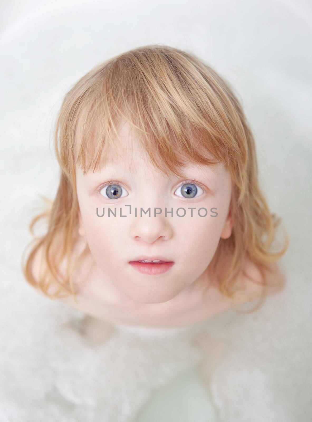 boy with long blong hair standing in bathtub looking up