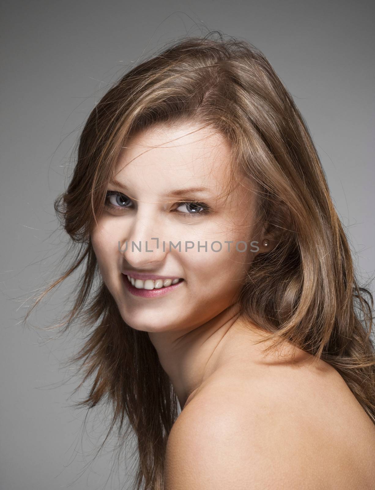 portrait of a young beautiful woman with brown hair against gray background