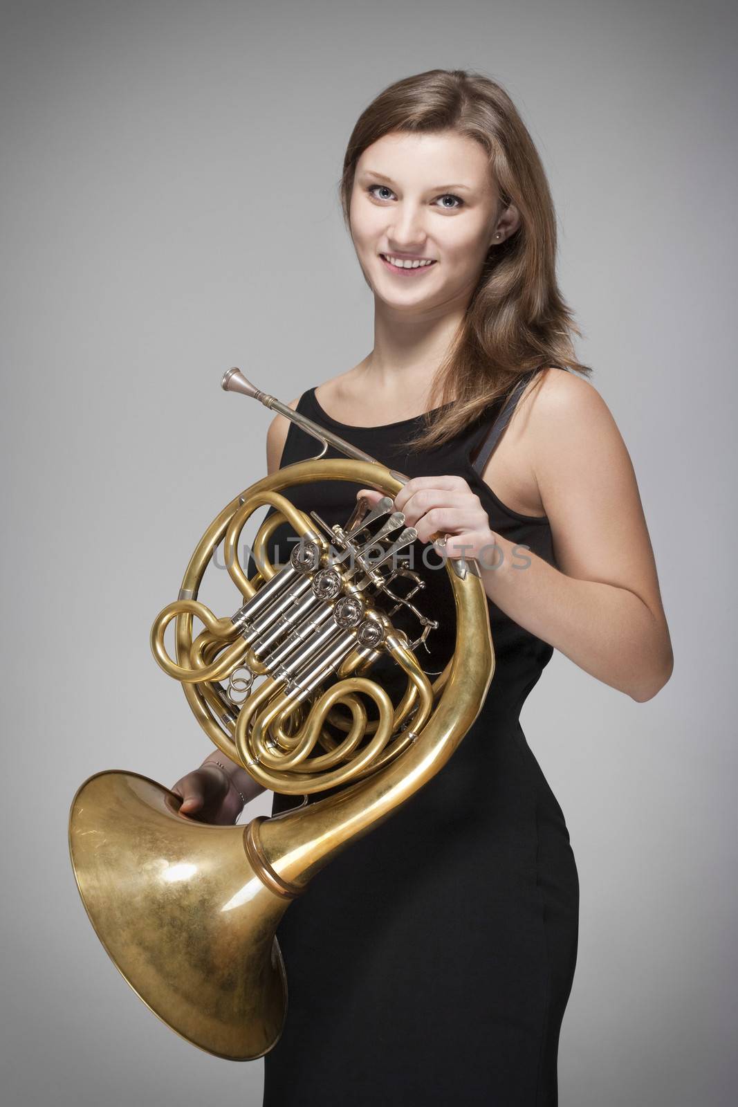 young female musician with concert french horn in black dress