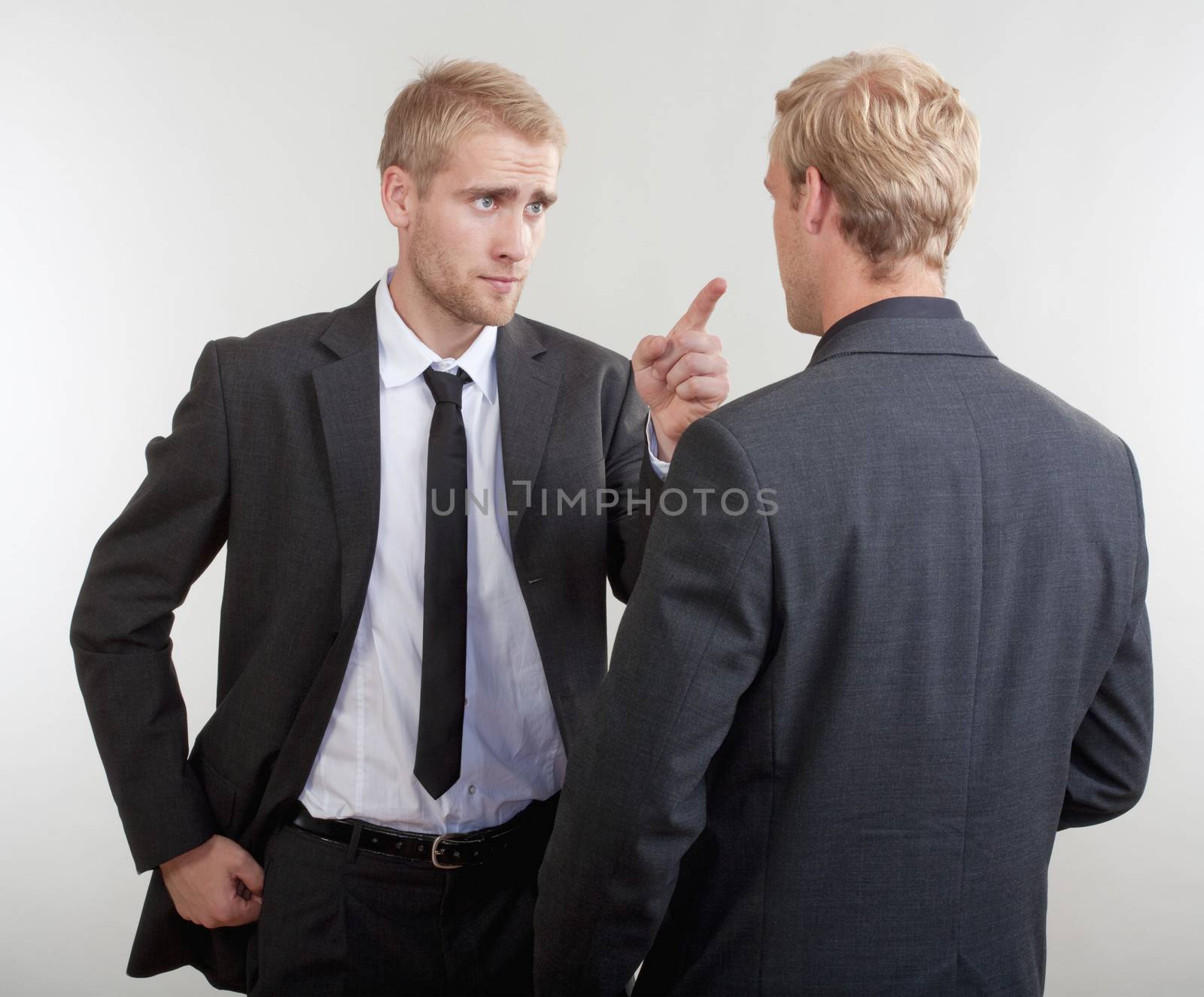 two young businessmen standing, discussing, arguing - isolated on light gray