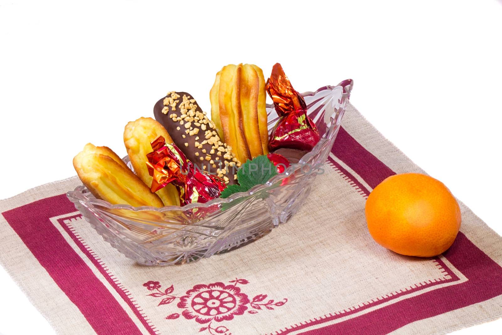 Crystal vase filled with cakes, sweets, Mandarin. Located on a napkin from flax. Presented on a white background..