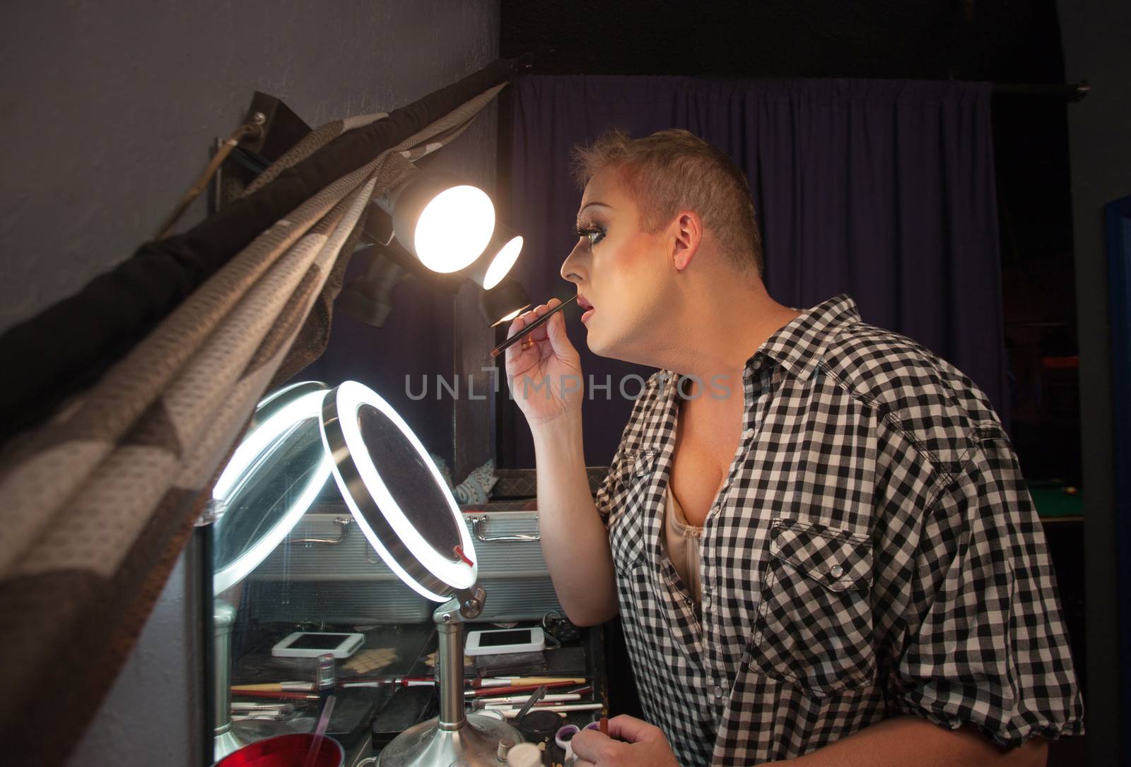 Serious male drag queen performer using lipstick pencil