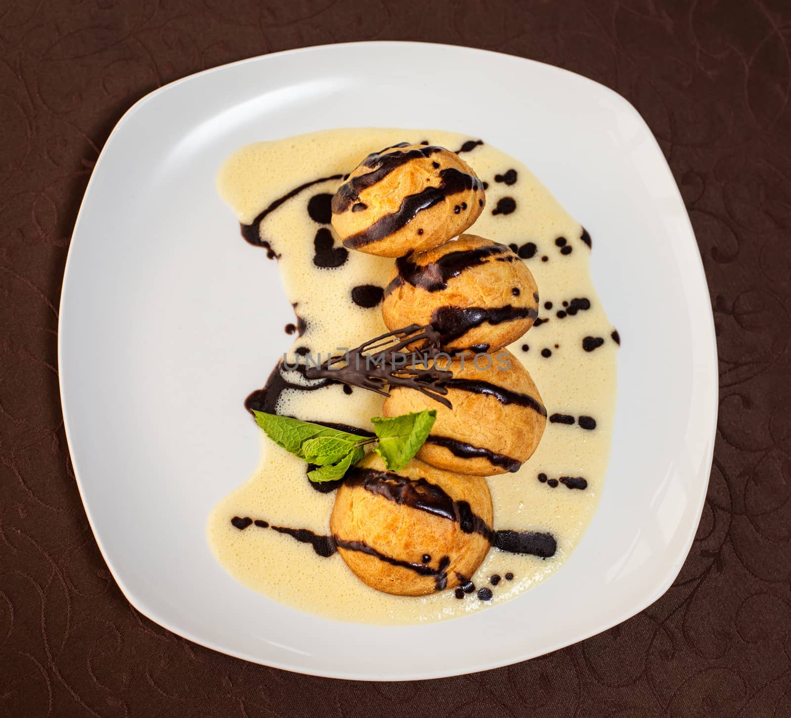 tasty dessert with chocolate, sweet sauce, cakes and mint on a white plate