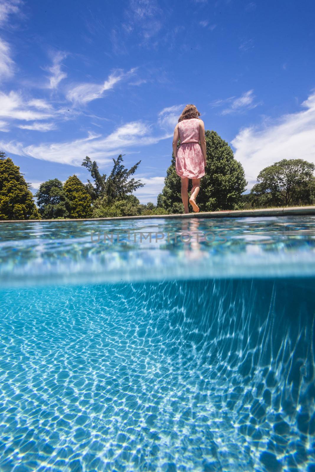 Girl testing pool water by dipping her tocsin to feel the temperature.