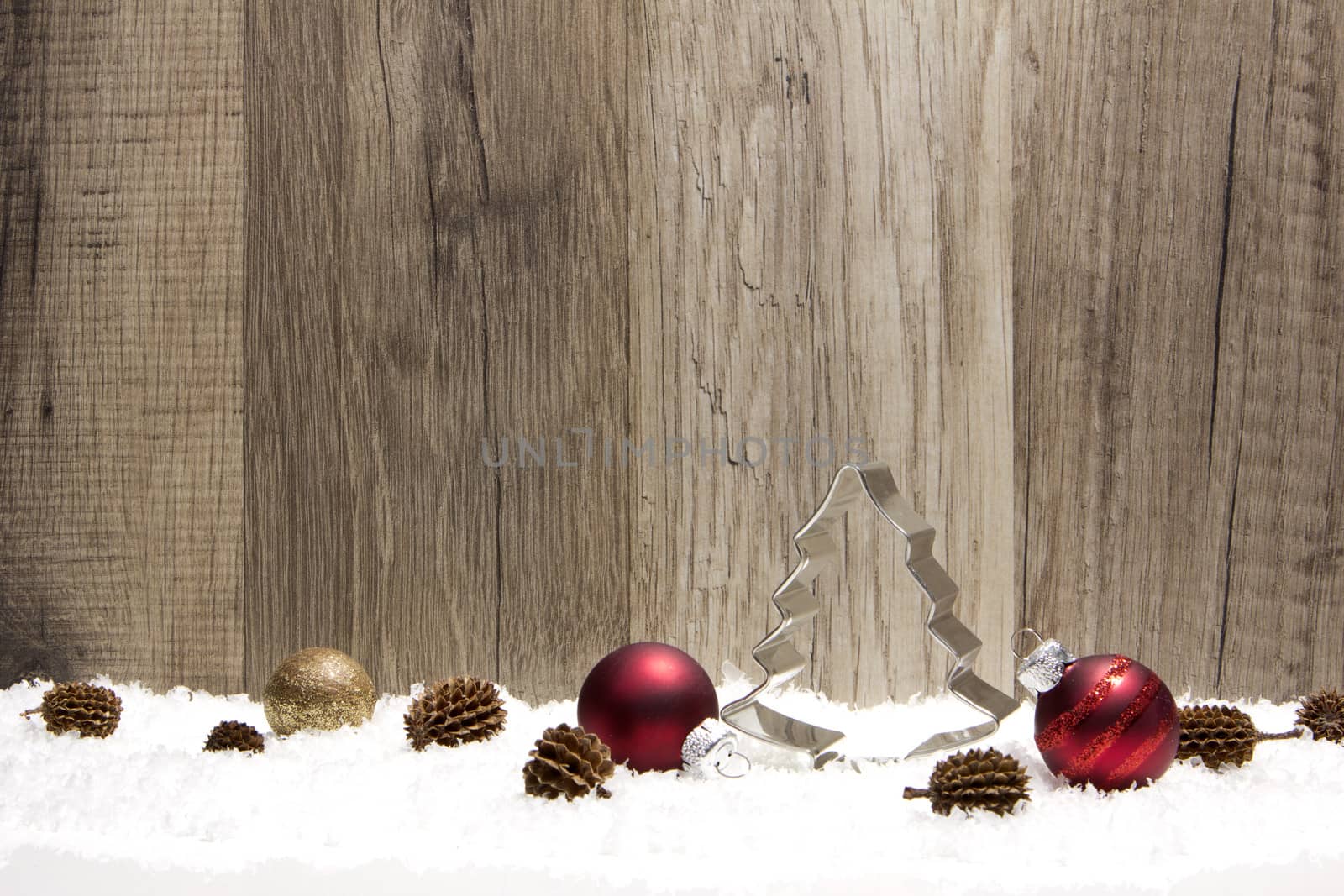 christmas decoration with wooden background, snow, christmas baubles red, gold and pine cones 
