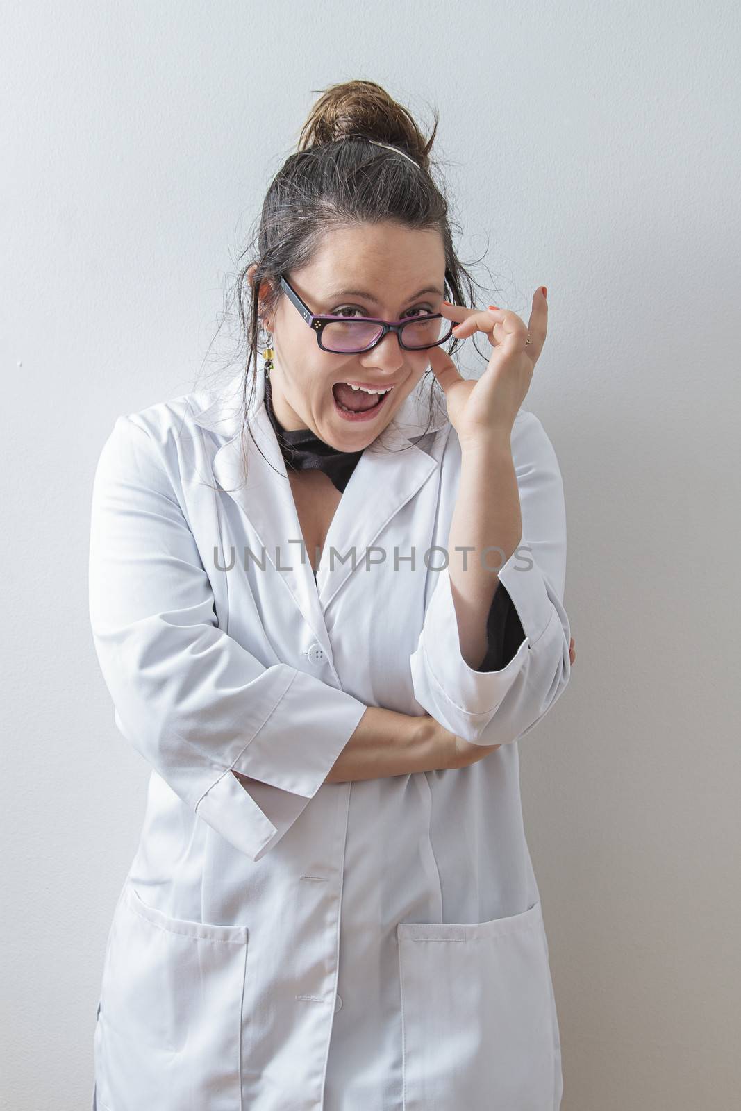 thirtie something brunette woman wearing a lab coat holding her glasses with a big funny smile