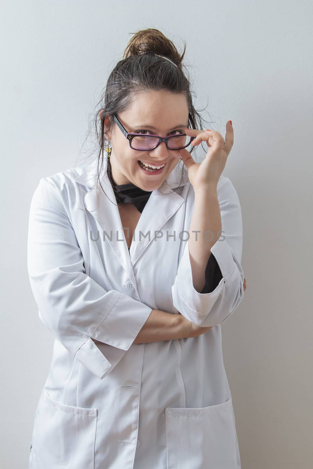 thirtie something brunette woman wearing a lab coat holding her glasses with a big funny smile