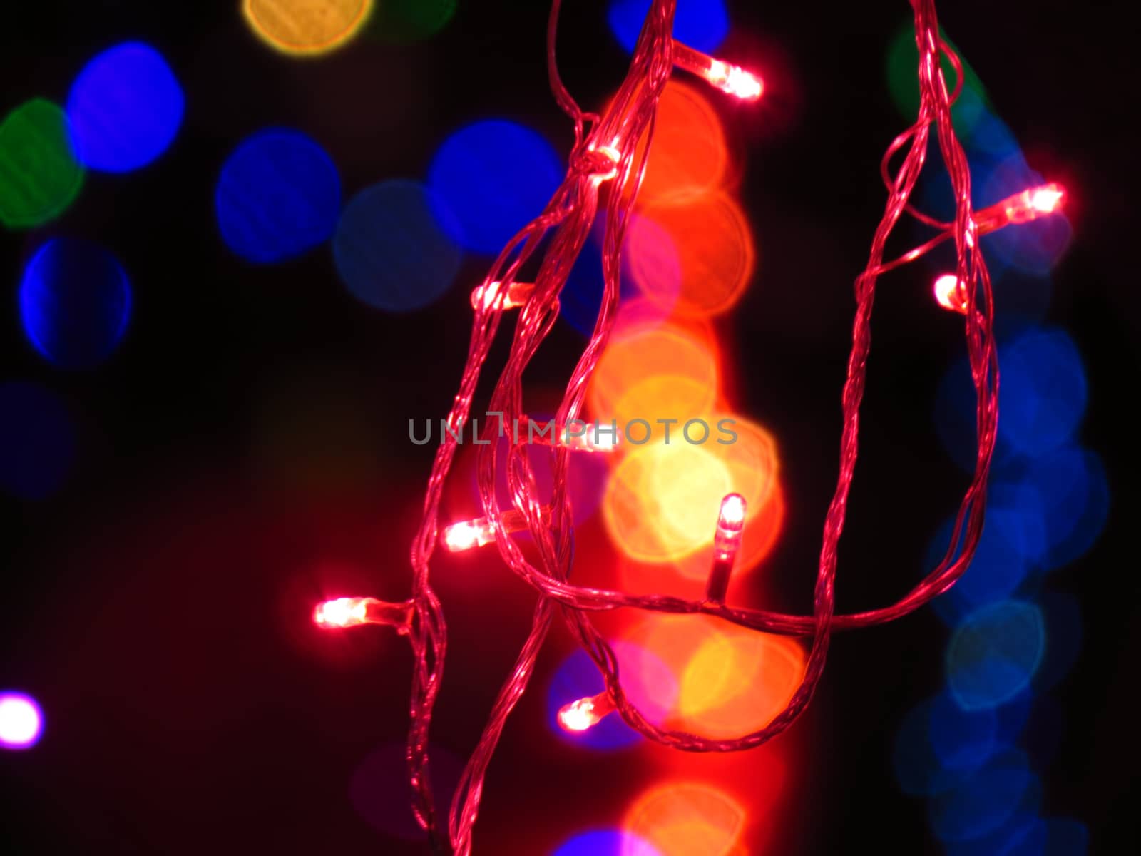A red light bulbs wire string on the backdrop of other colors blurred light for festive Christmas or Diwali decoration.