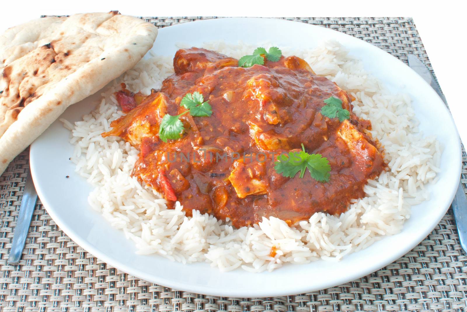Plate of chicken curry with coriander and naan bread on the side 