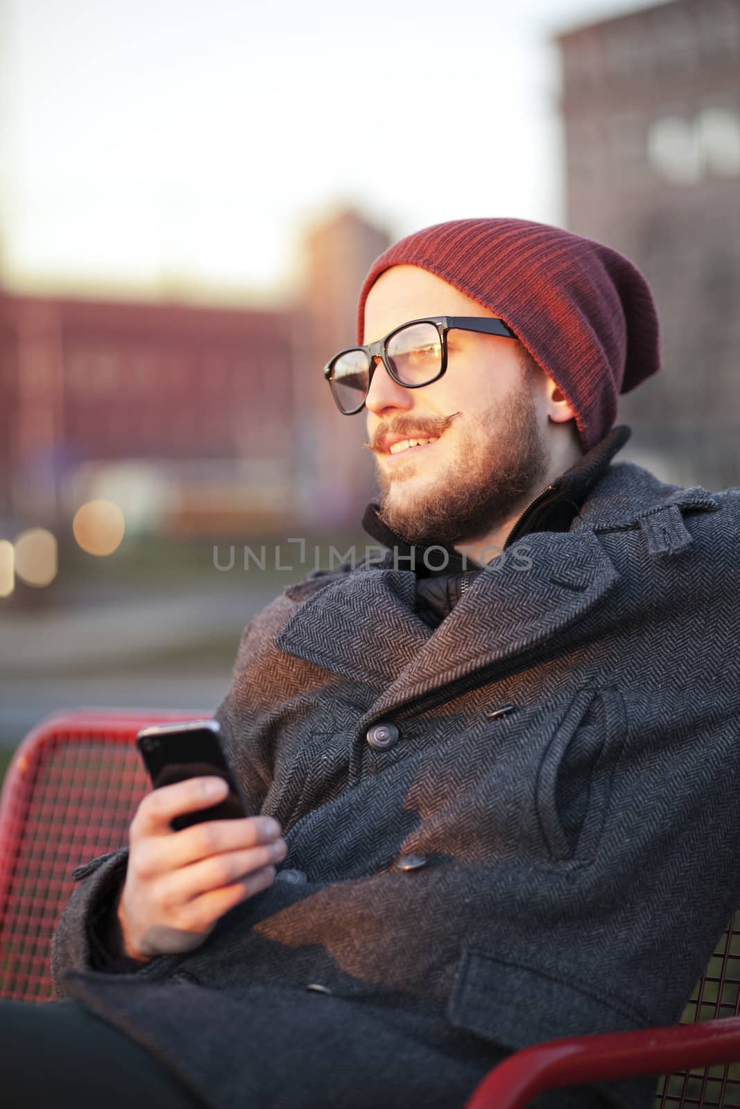 Young smiling man with smartphone on the city bench