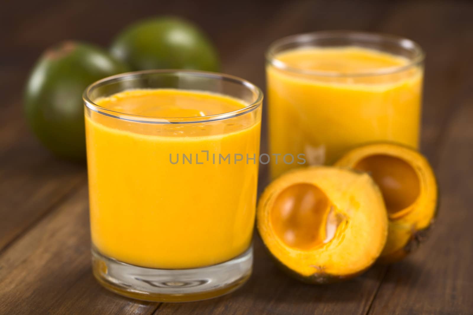 Milkshake made of the Peruvian fruit called lucuma (lat. Pouteria lucuma) served in glass with lucuma fruits around (Selective Focus, Focus on the front of the glass rim) 