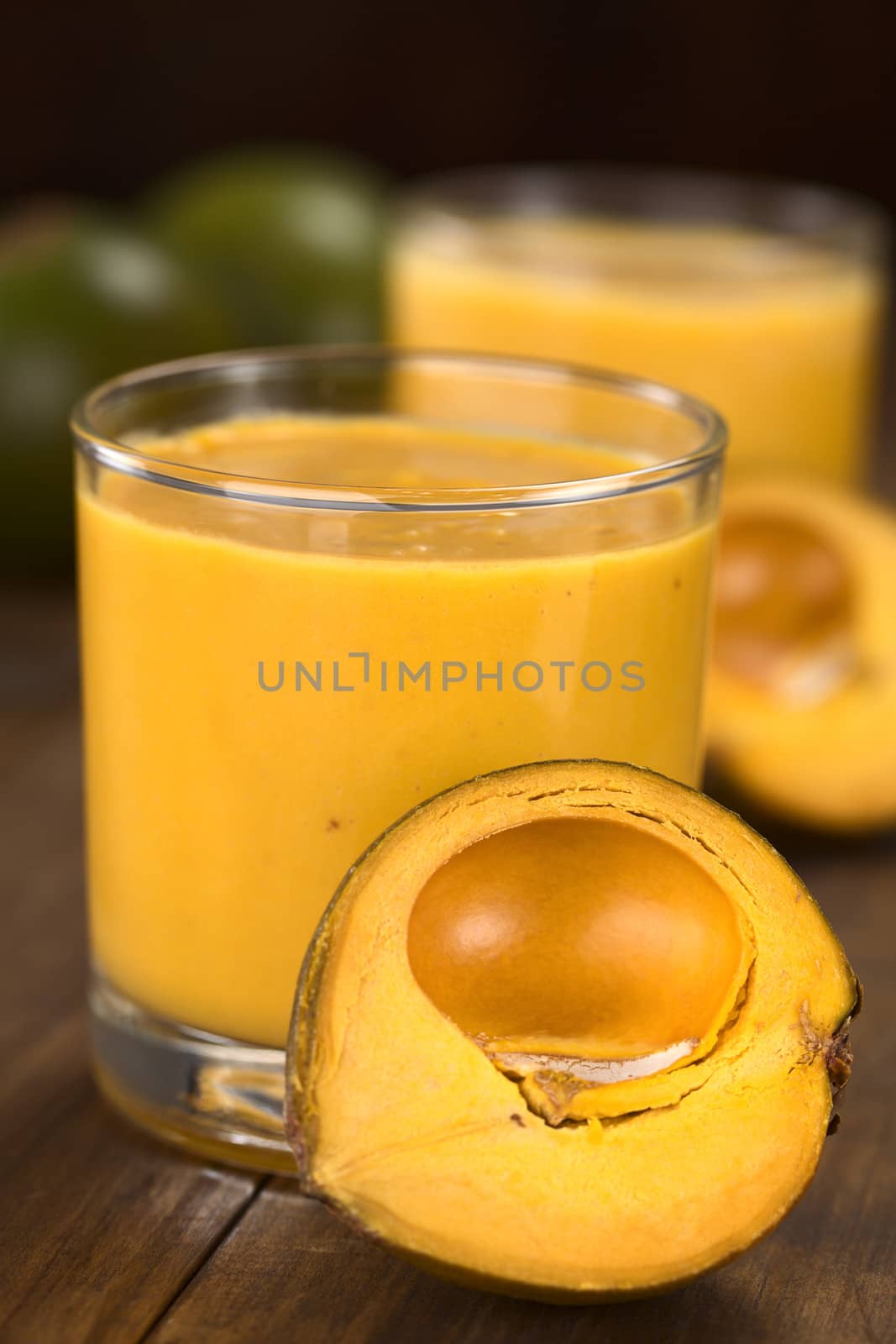 Milkshake made of the Peruvian fruit called lucuma (lat. Pouteria lucuma) served in glass with lucuma fruits around (Selective Focus, Focus on the front of the glass rim and the upper part of the lucuma in the front) 