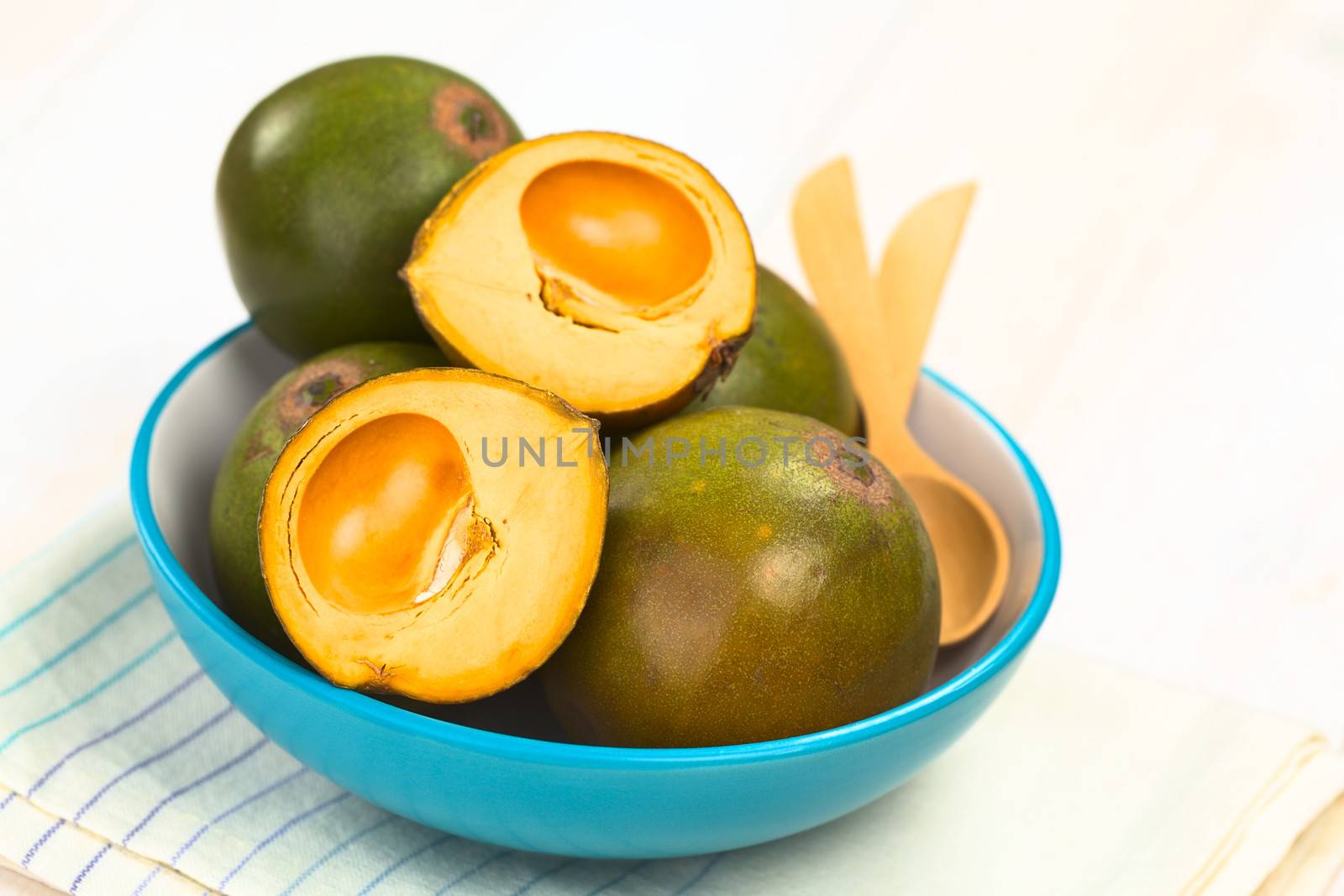 Peruvian fruit called Lucuma (lat. Pouteria lucuma), which has a dry, sweet flesh, and is mostly used to prepare juices, milkshakes, yogurts, ice cream and other desserts, served in a blue bowl (Selective Focus, Focus on the front of the first fruits) 