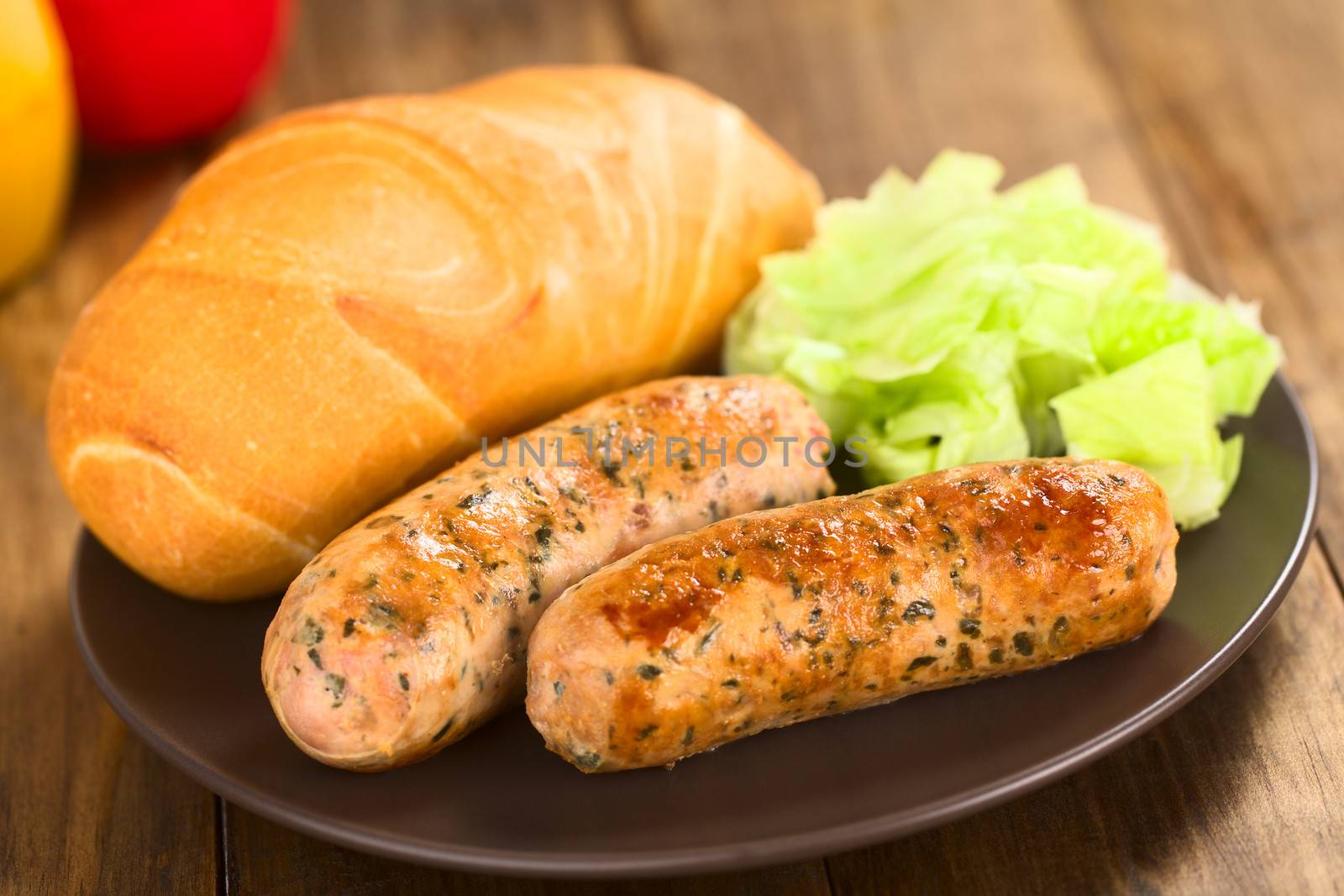 Fried bratwurst with bun, traditional German fast food served on plate with green salad (Selective Focus, Focus on the right side of the right bratwurst)