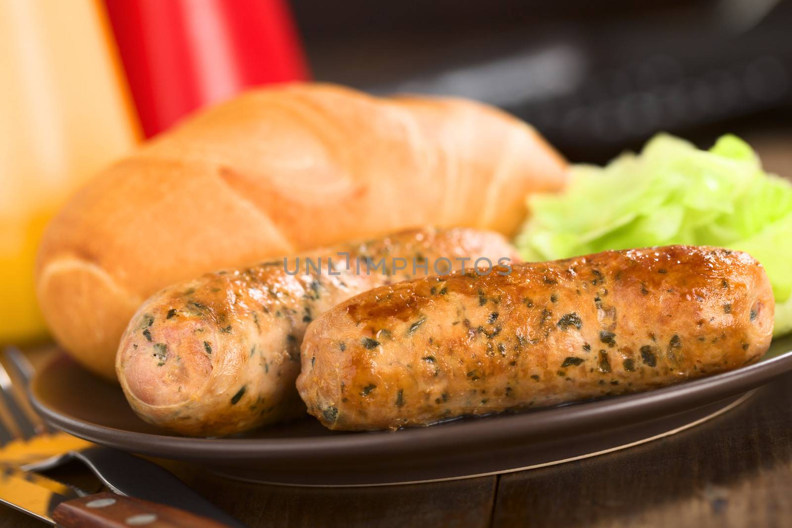 Fried bratwurst with bun, traditional German fast food served on plate with green salad (Selective Focus, Focus on the front of the first bratwurst)