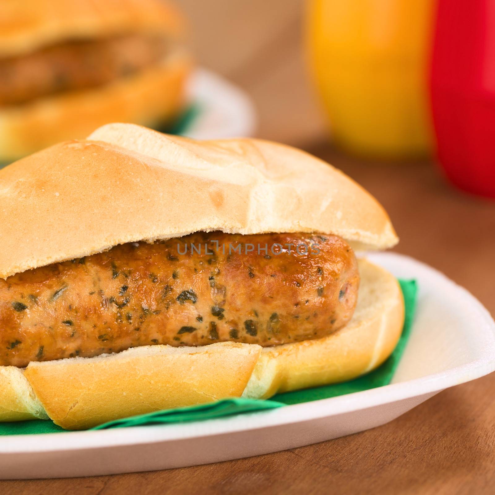 Fried bratwurst in bun, traditional German fast food served on disposable plate with napkin, ketchup and mustard in the back (Selective Focus, Focus on the front of the bratwurst)