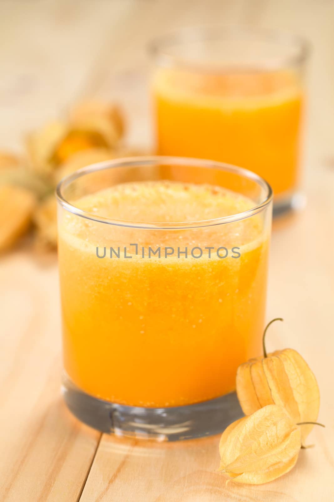 Freshly prepared juice made of physalis (lat. Physalis peruviana) served in glass with physalis fruits on the side (Selective Focus, Focus on  the front of the glass rim and on the front of the first physalis next to the glass)
