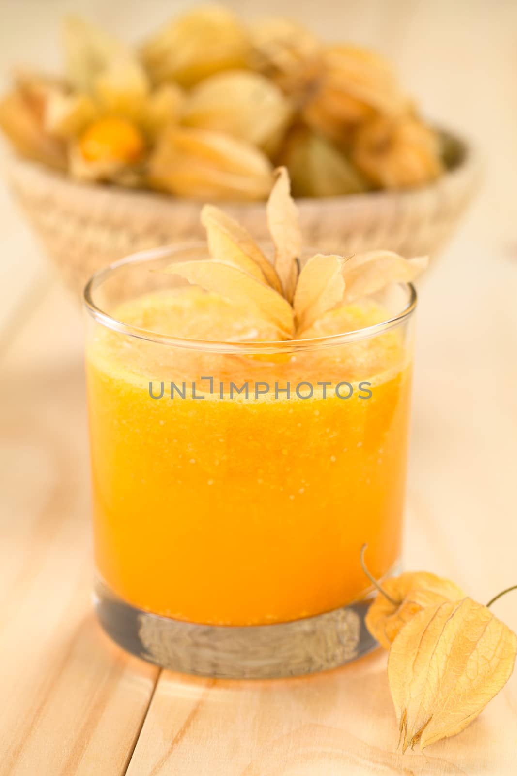 Freshly prepared juice made of physalis (lat. Physalis peruviana) served in glass with physalis fruits on the side and a basket full of physalis in the back (Selective Focus, Focus on  the front of the glass rim and on the front of the first physalis next to the glass)
