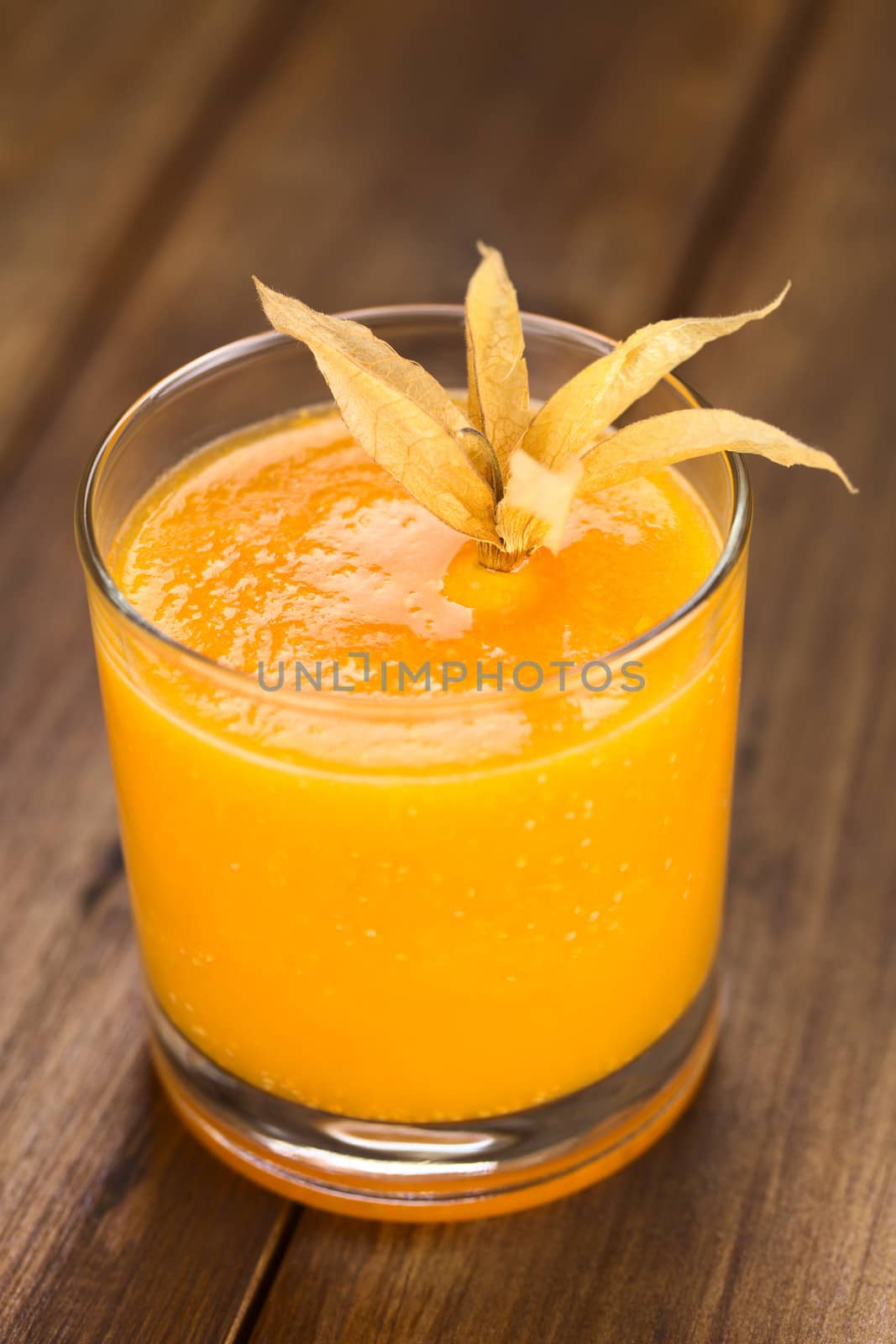 Freshly prepared juice made of physalis (lat. Physalis peruviana) served in glass garnished with a physalis (Selective Focus, Focus in the middle of the juice)

