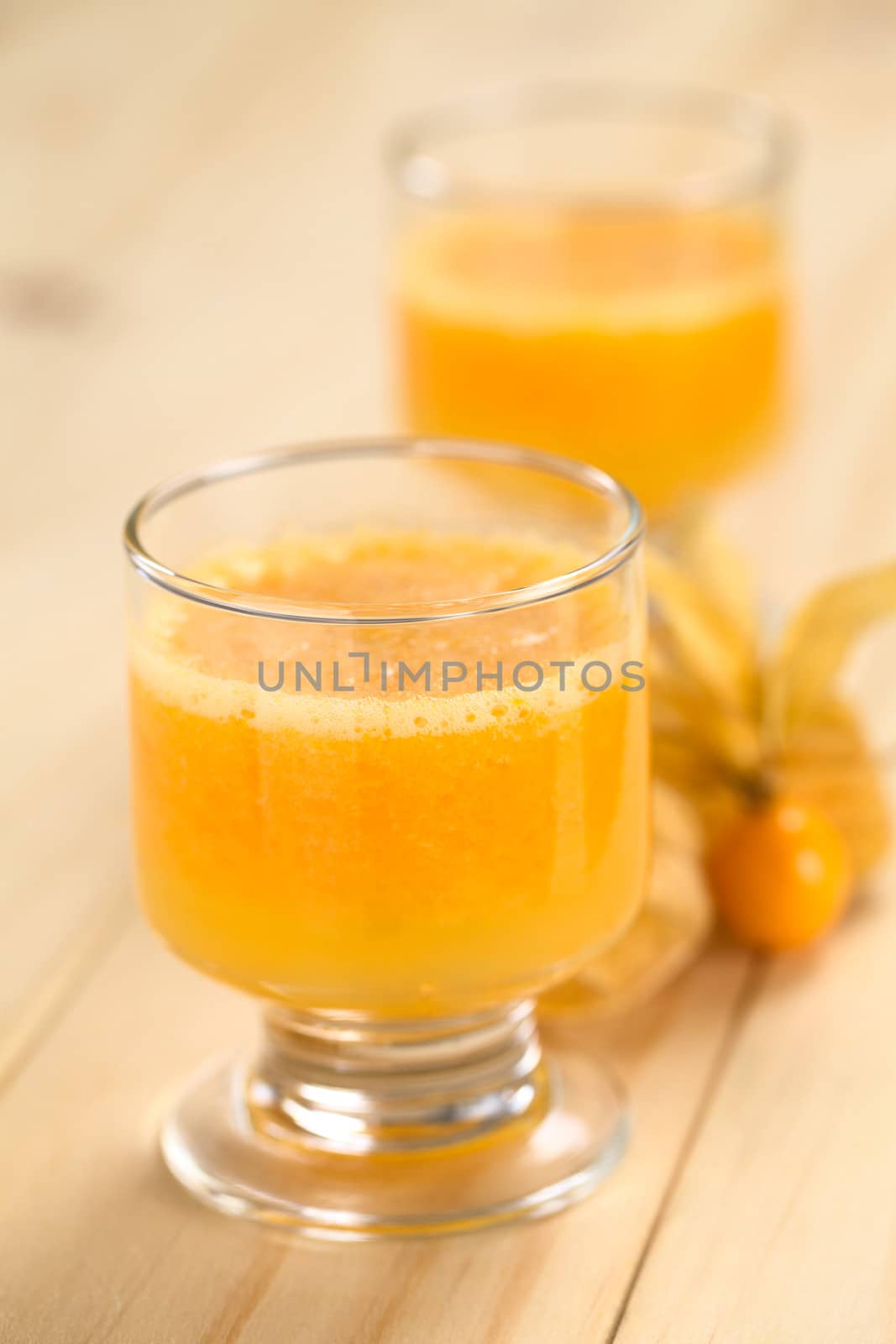 Freshly prepared juice made of physalis (lat. Physalis peruviana) served in glass with physalis fruits on the side (Selective Focus, Focus on  the front of the glass rim)

