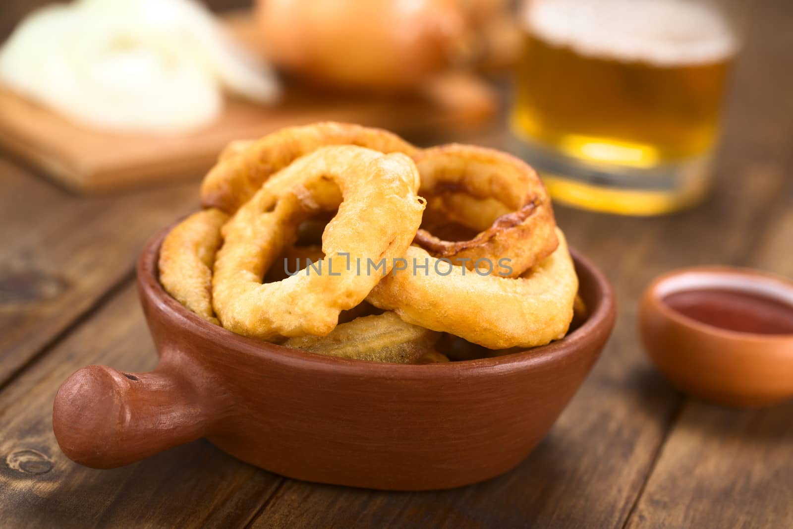 Freshly prepared homemade beer-battered onion rings in a rustic bowl with ketchup on the side (Selective Focus, Focus on the front of the onion ring on the right)