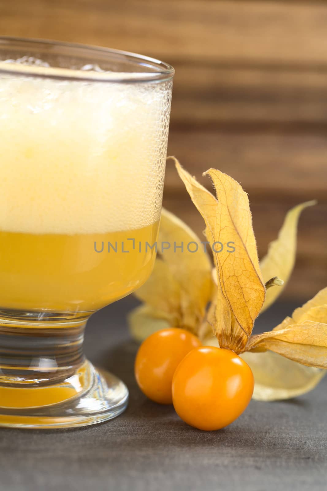 Physalis berries (lat. Physalis peruviana) with a Peruvian cocktail called Aguaymanto Sour (Physalis Sour) prepared from physalis juice, pisco (Peruvian grape hard liquor), syrup and egg white on the side (Selective Focus, Focus on the front of the first physalis berry) 