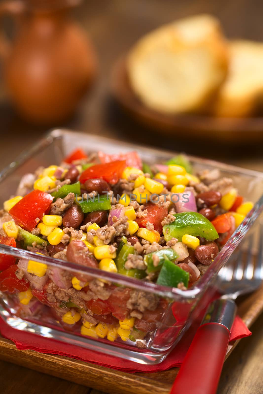 Chili con carne salad made of mincemeat, kidney beans, green bell pepper, tomato, sweet corn and red onions served in glass bowl (Selective Focus, Focus one third into the salad)