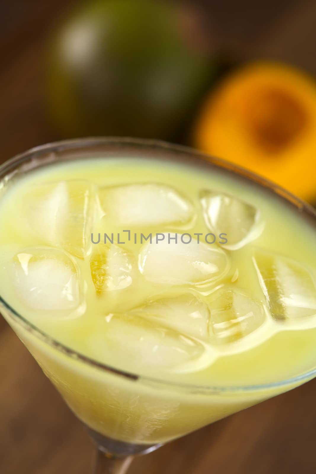 Peruvian cream liqueur made of lucuma fruit served in cocktail glass with ice cubes, lucuma fruit in the back (Selective Focus, Focus in the middle of the ice cubes)