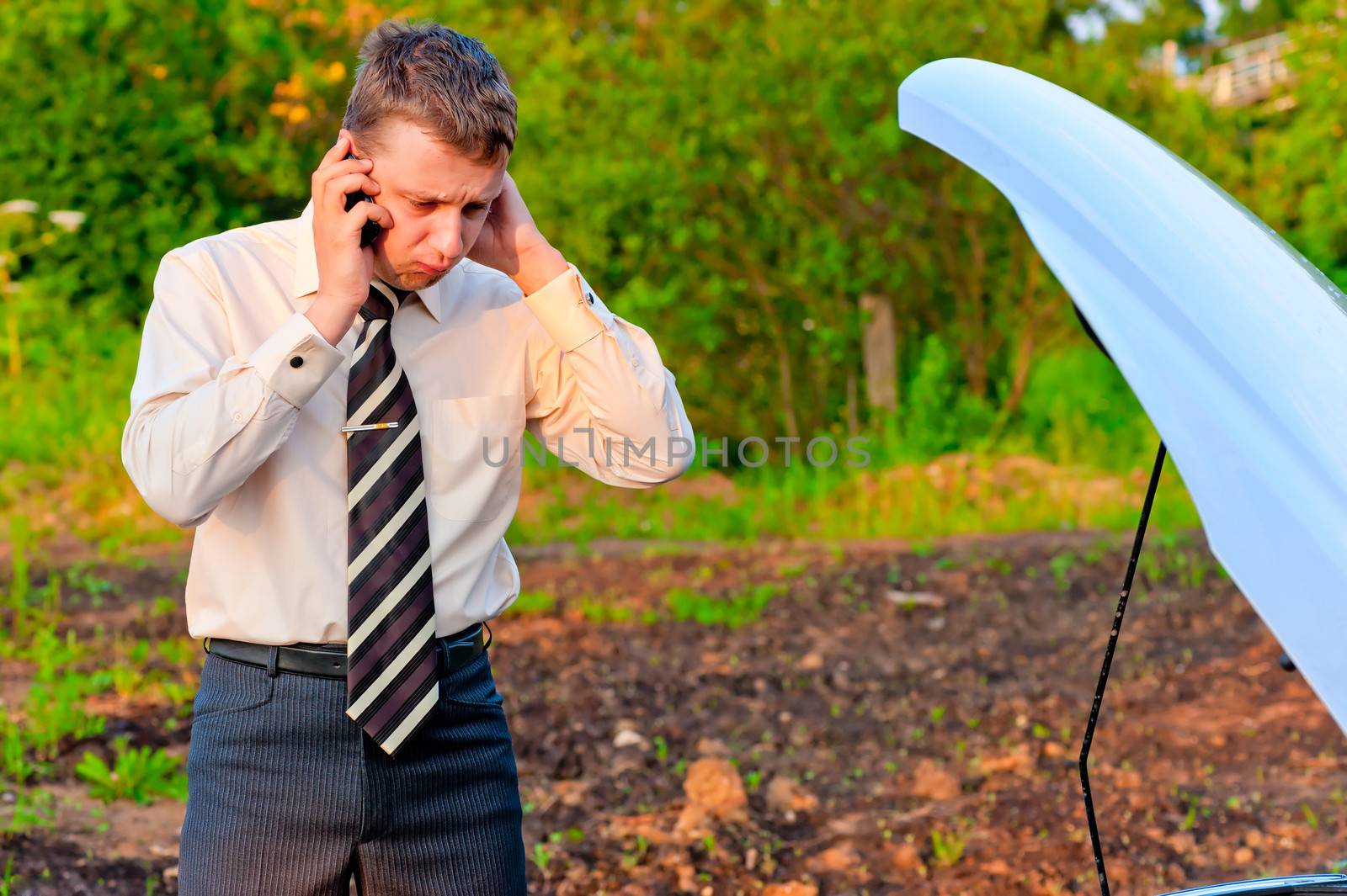 businessman talking on the phone near the broken car