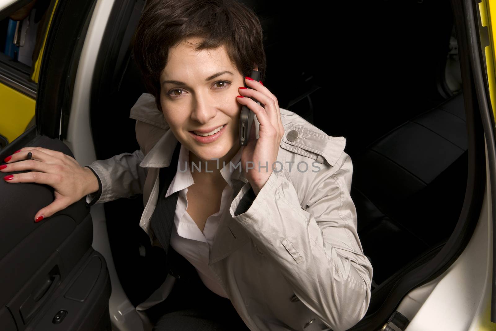 A woman smiling as she gets out of taxi cab simultaniously talking on cell phone