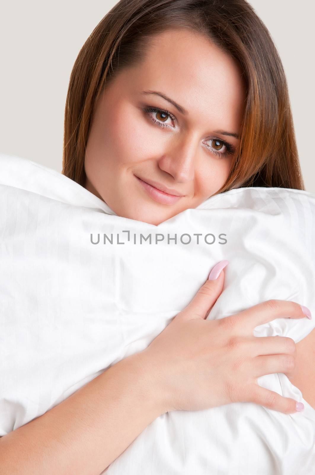 Woman holding a white pillow, isolated in a grey background