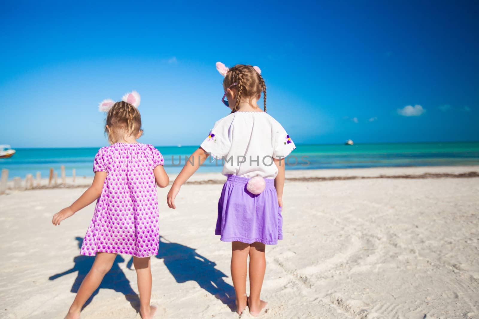 Two little cute girls in easter ears have fun on the exotic beach by travnikovstudio