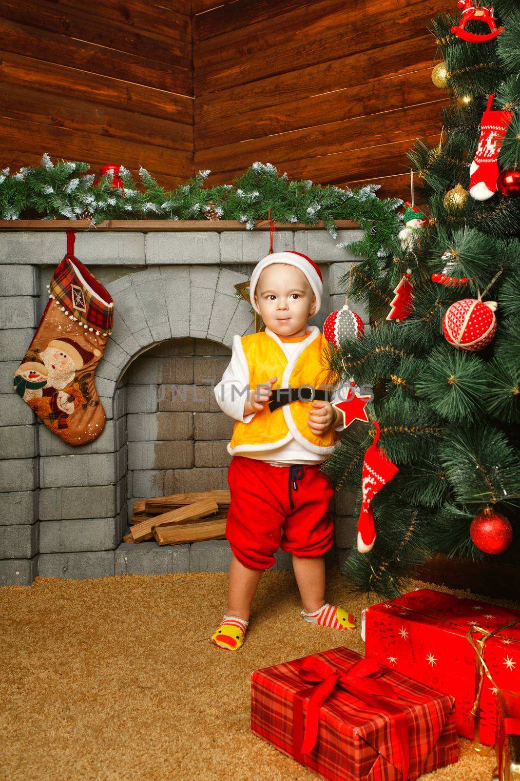 Child standing near Christmas tree beneath which lie gifts