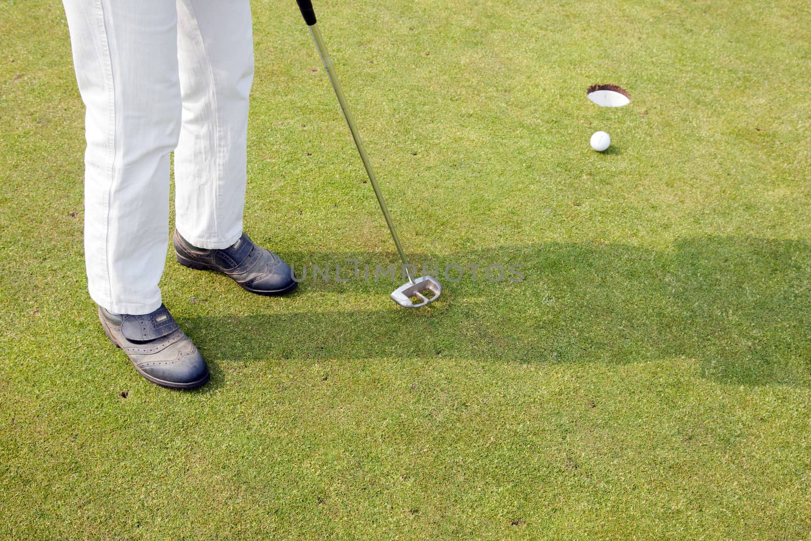 female in white trousers tries to putt the ball on the green of golf field