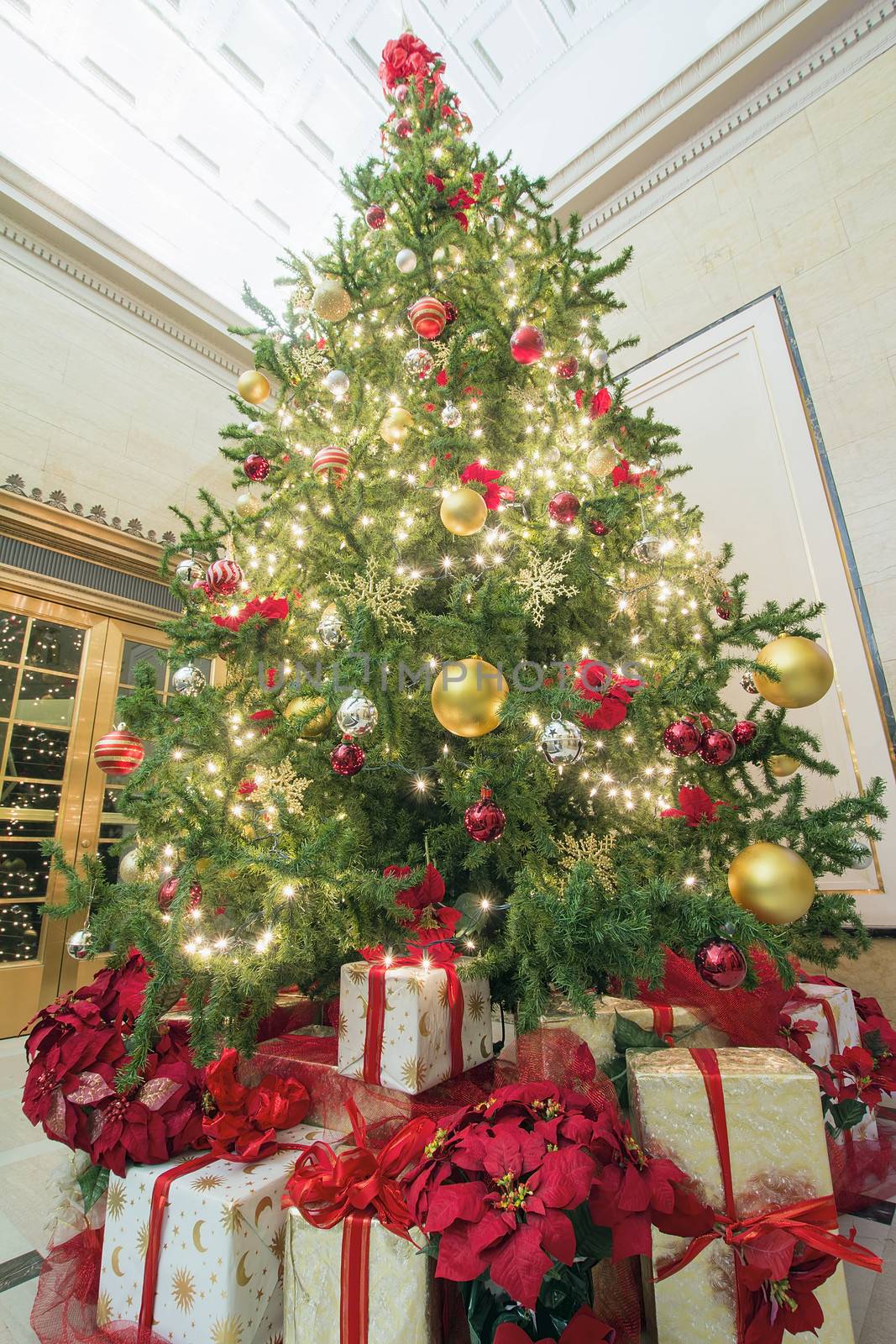 Christmas Tree Decoration with Bokeh Lights Ornaments Ribbons Poinsettia and Presents Under the Tree Tall Perspective