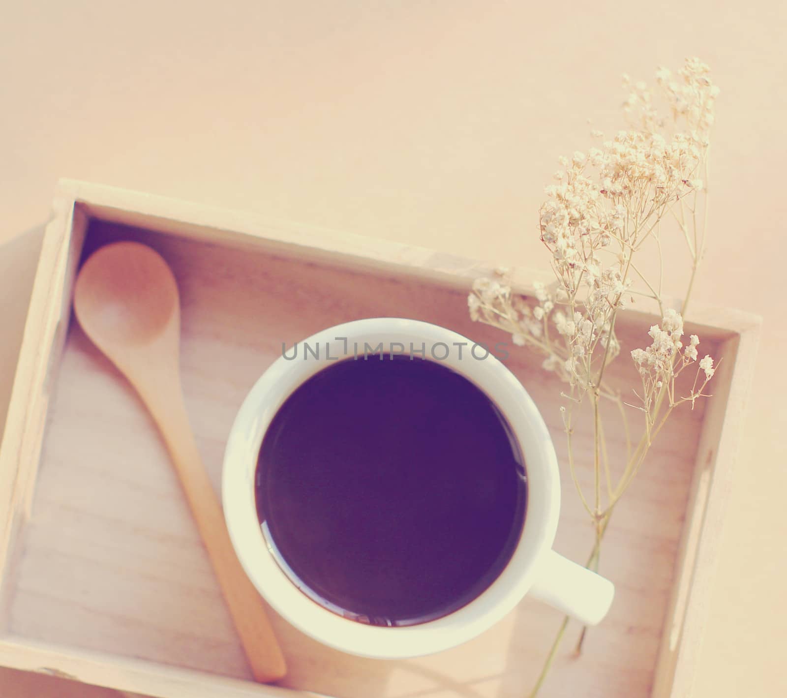 Black coffee and spoon on wooden tray with dried flower, retro filter effect