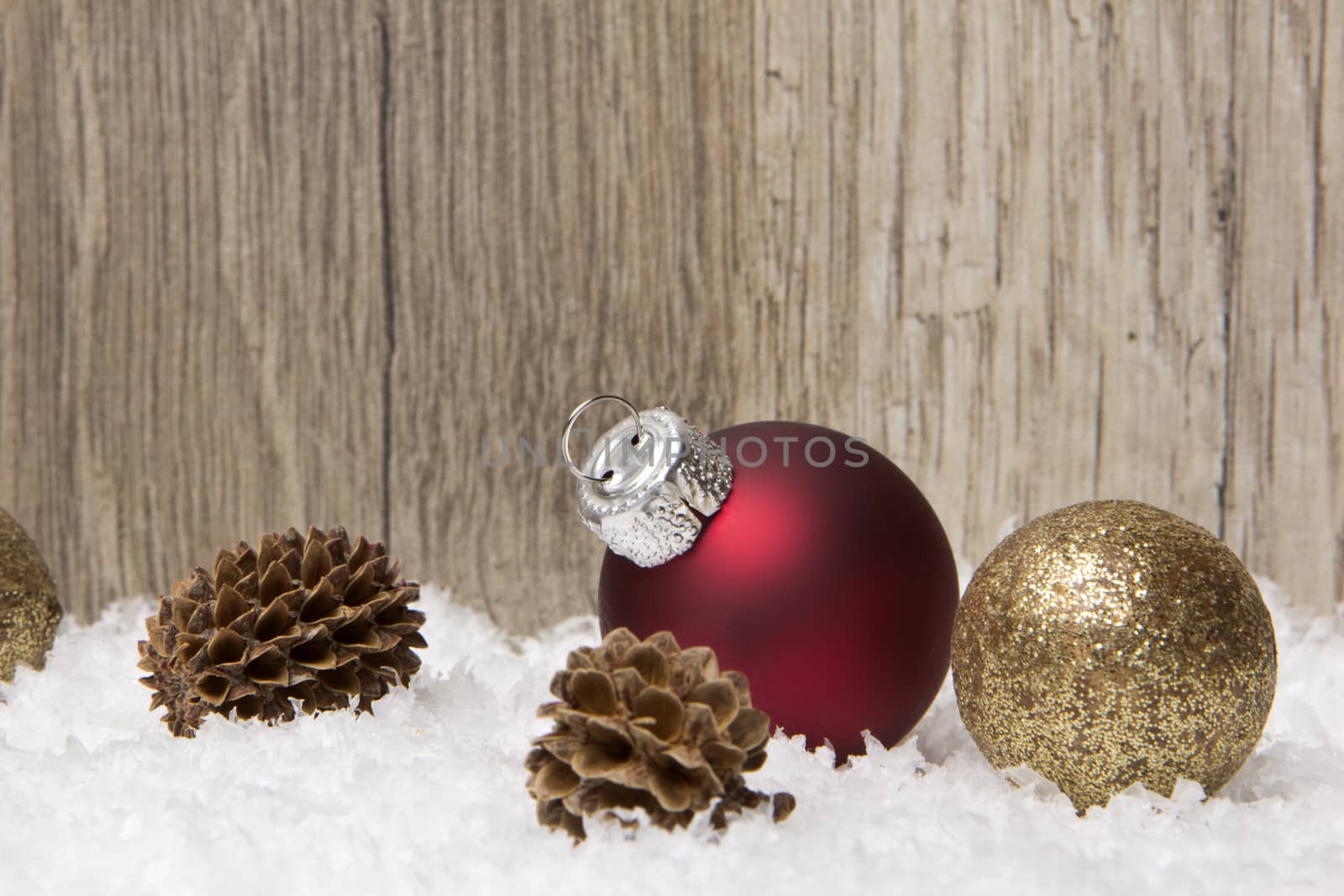 christmas decoration with wooden background, snow, christmas baubles red, gold and pine cones 