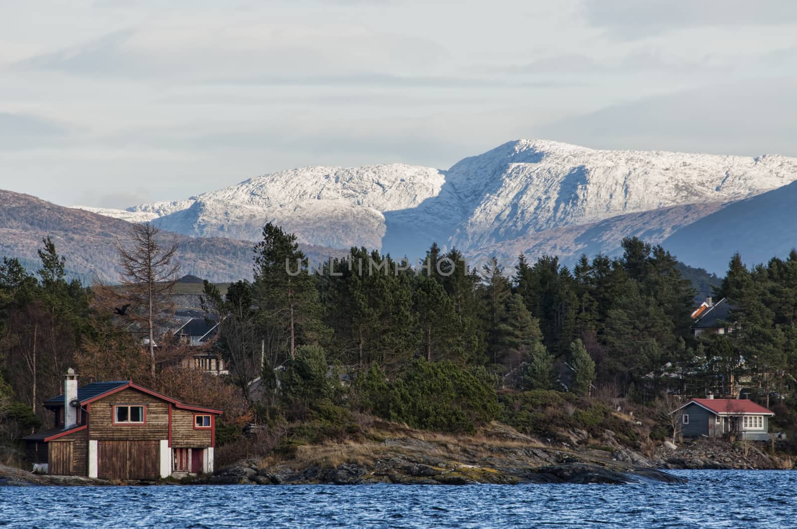 Cabins by the coast with mountains covered in snow in the background
