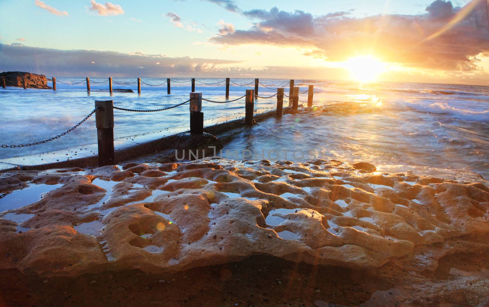 Golden rays of sunlight emerge at sunrise at the idyllic Mahon pool located on exposed rock shelf at Maroubra, Sydney Australia