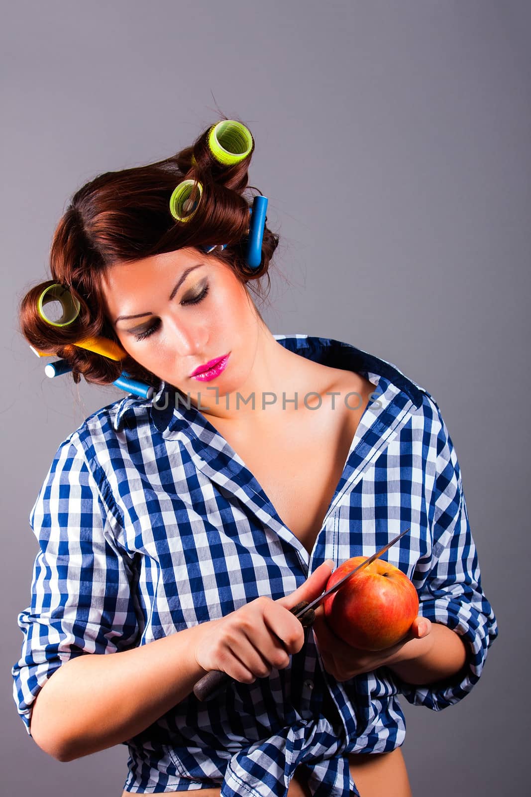 portrait of beautiful housewife with curlers holding apple and the knife