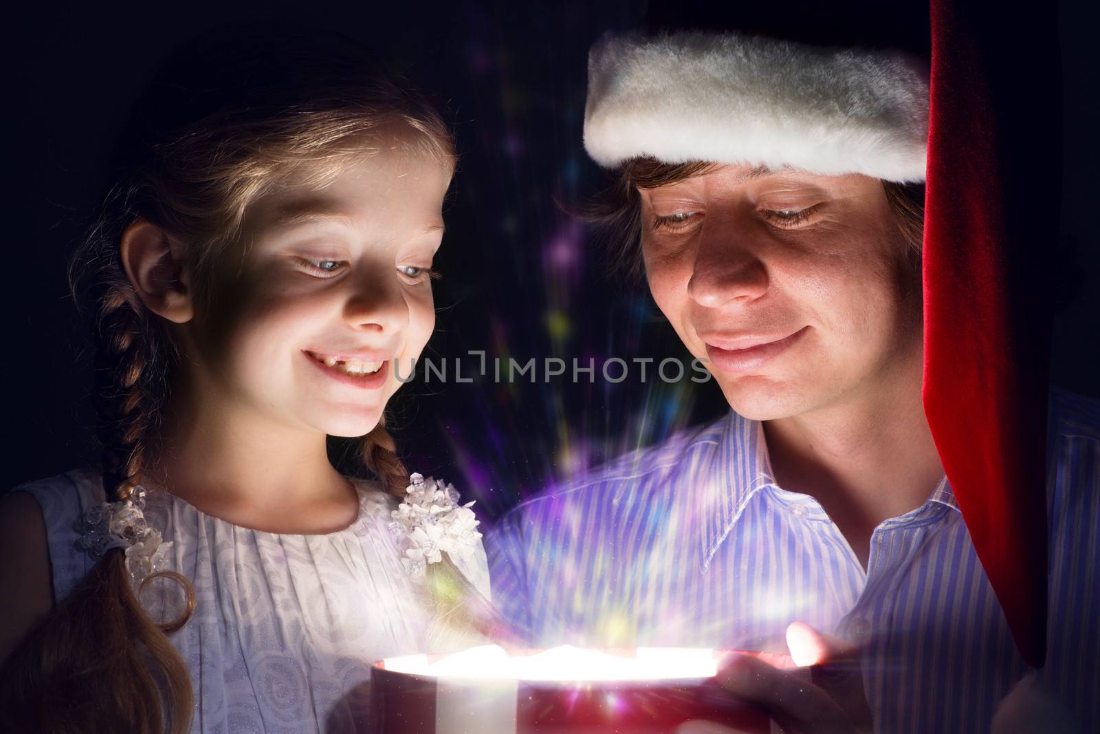 father in Santa Claus cap and daughter opened a box with Christmas gift boxes of shining light and magic